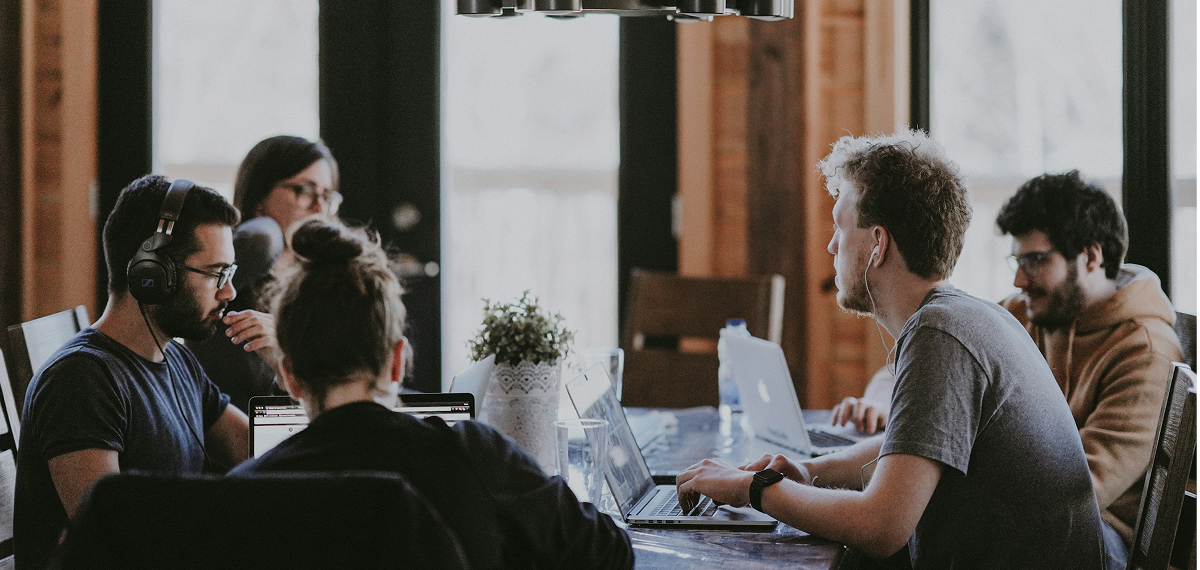 a group of people sitting at a table with laptops