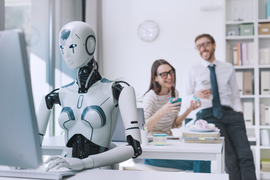 a robot sitting at a desk with a woman in the background